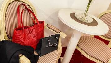 A chair with a striped cushion, a red handbag, a black shopping bag, and a small table with a vase of flowers.