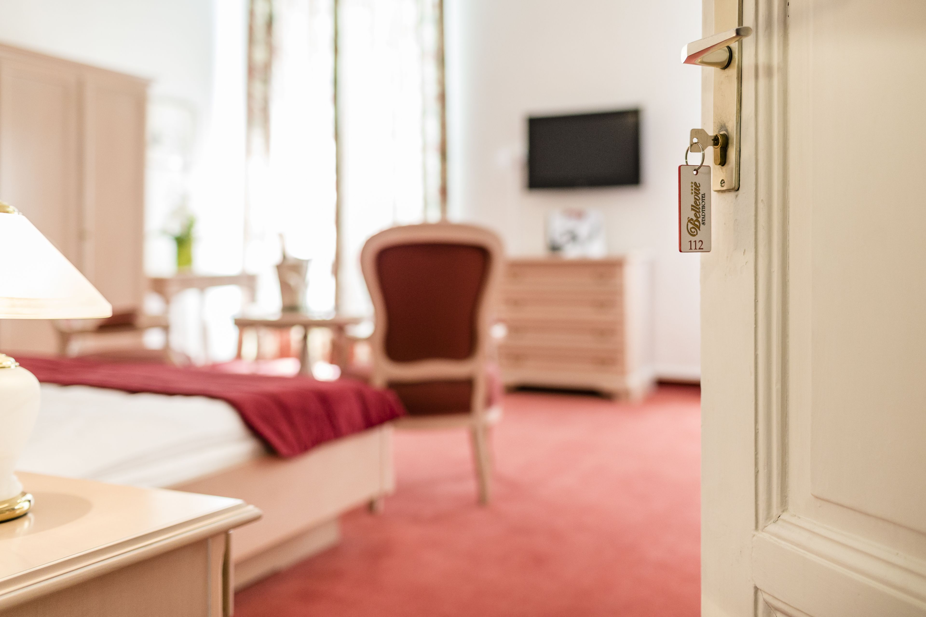 Habitación de hotel con cama, mesita de noche, silla, cómoda y televisor en la pared.