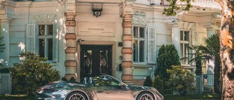 A luxury car parked in front of a grand hotel with a classic facade and columns.