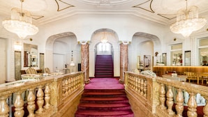 A grand staircase with marble railings and a red carpet leading to a high-ceilinged area with chandeliers. - Grand Hotel Bellevue - adults only (Merano)