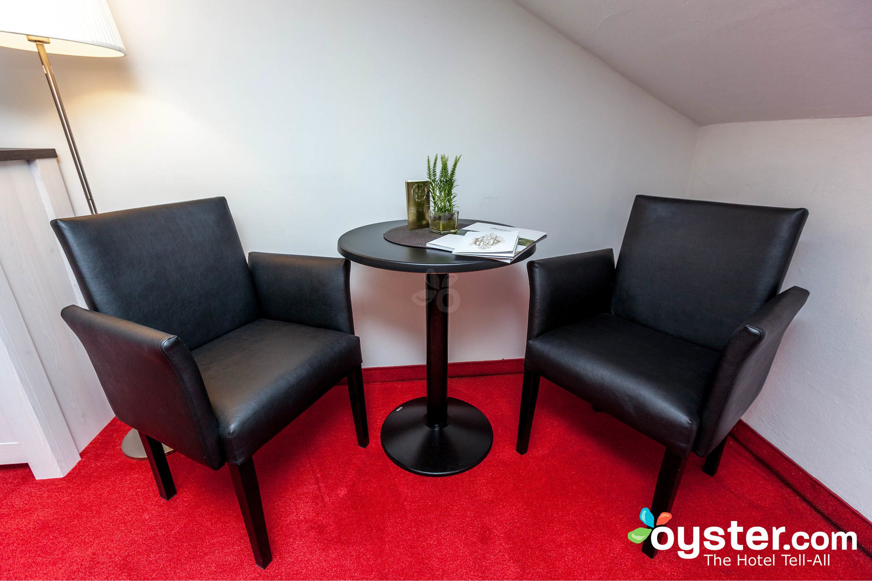 A small room with two black leather chairs, a round table, and a red carpet.