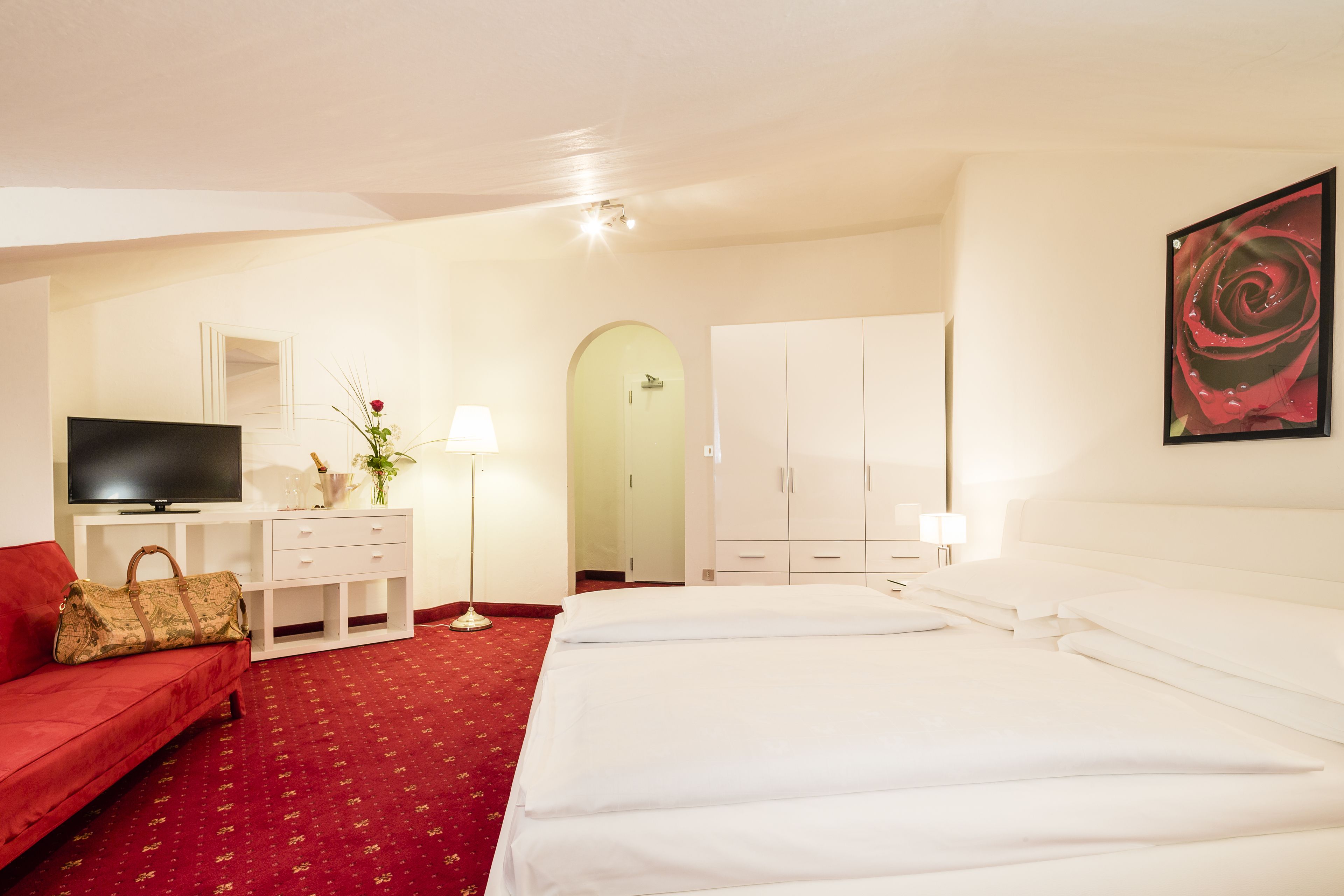 Une chambre d’hôtel avec un canapé rouge, une télévision, un bureau avec une lampe, un lit et une armoire.
