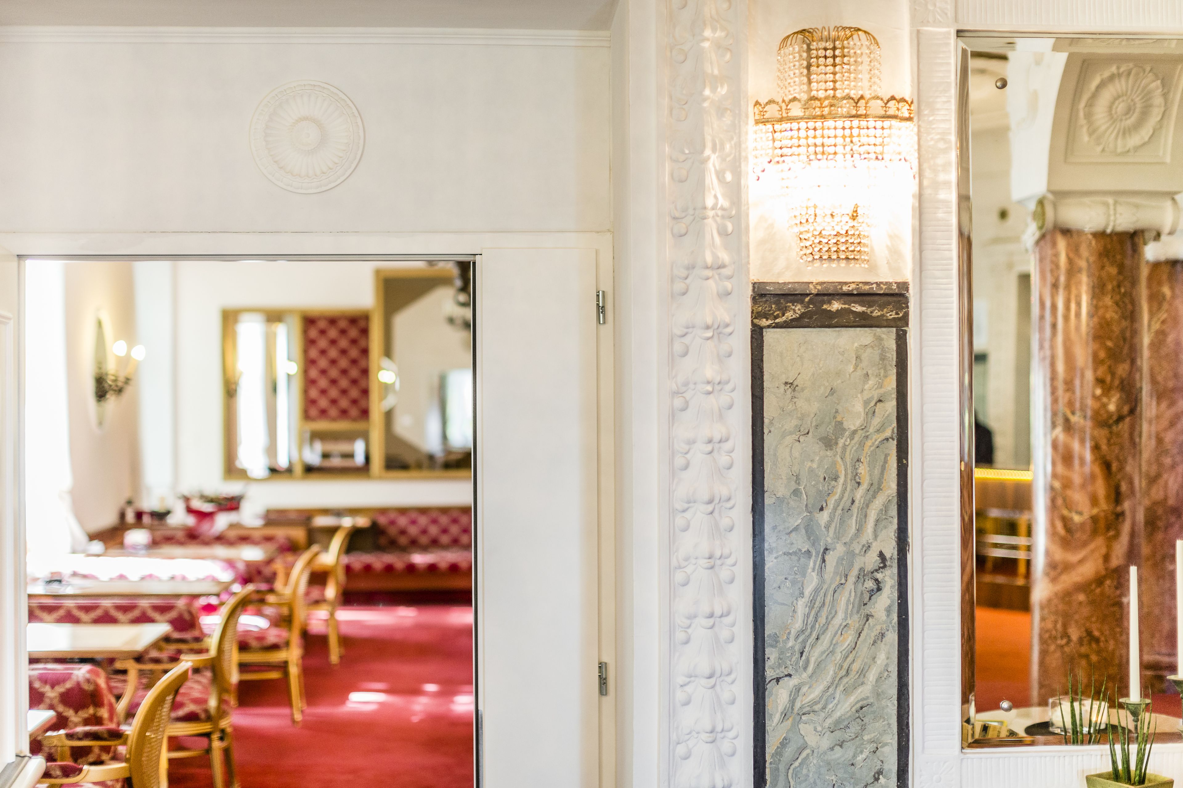 Un'elegante hall d'albergo con tappeto rosso, colonne di marmo e un lampadario.