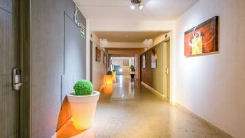 A hotel hallway with a modern design, featuring a potted plant, a door with a handle, and a wall-mounted sign.