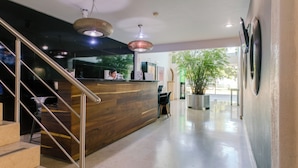 Un espace d’accueil avec un comptoir de réception en bois, un escalier avec des rampes en métal et une grande plante en pot.