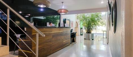 A reception area with a wooden reception desk, a staircase with metal railings, and a large potted plant.