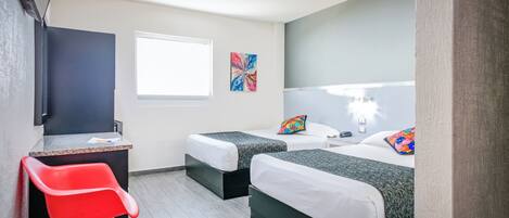 Habitación de hotel con dos camas, un escritorio, una silla, un ventanal y obras de arte en las paredes.