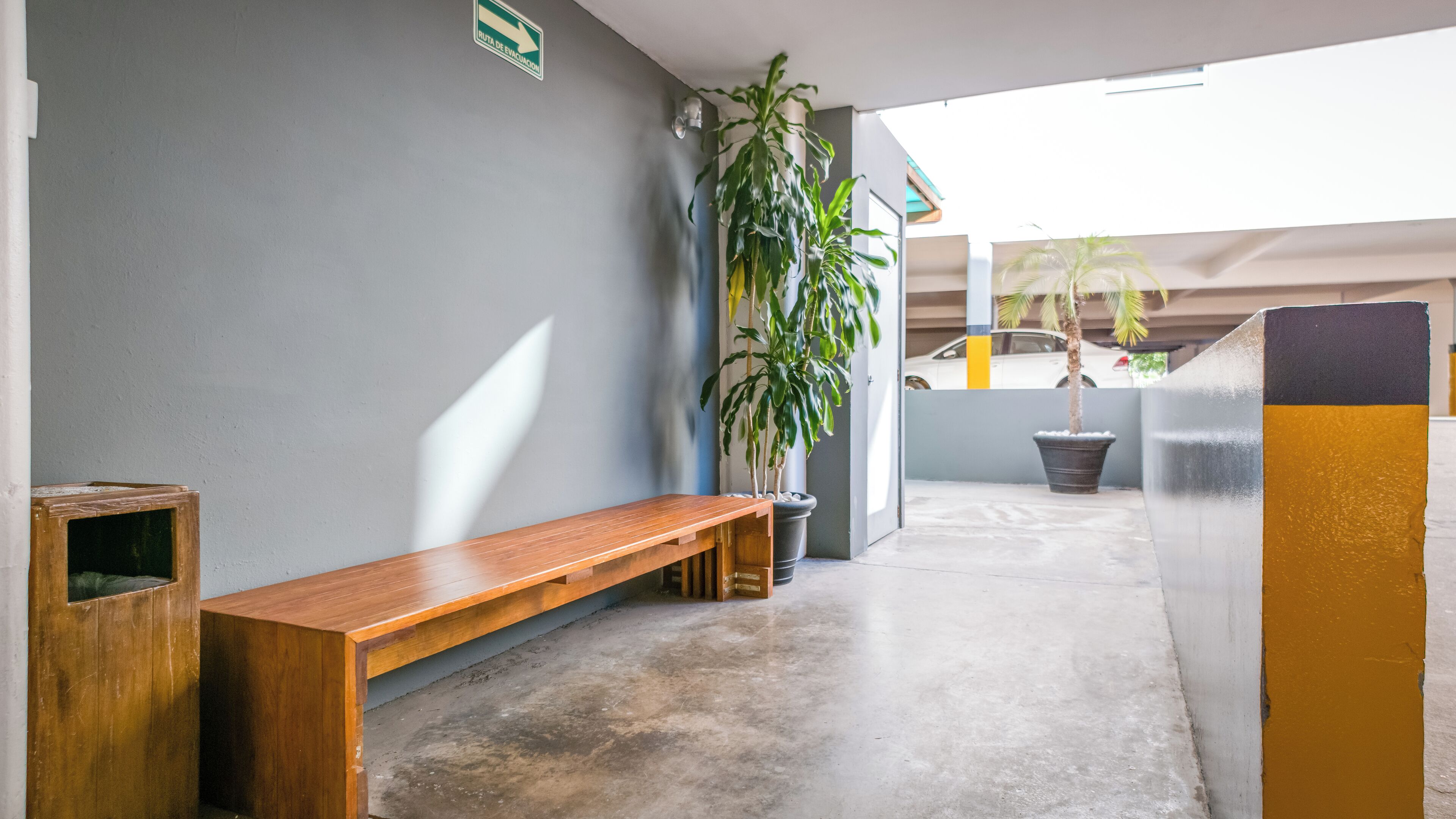 A hallway with a wooden bench, a potted plant, and a sign indicating an evacuation route.