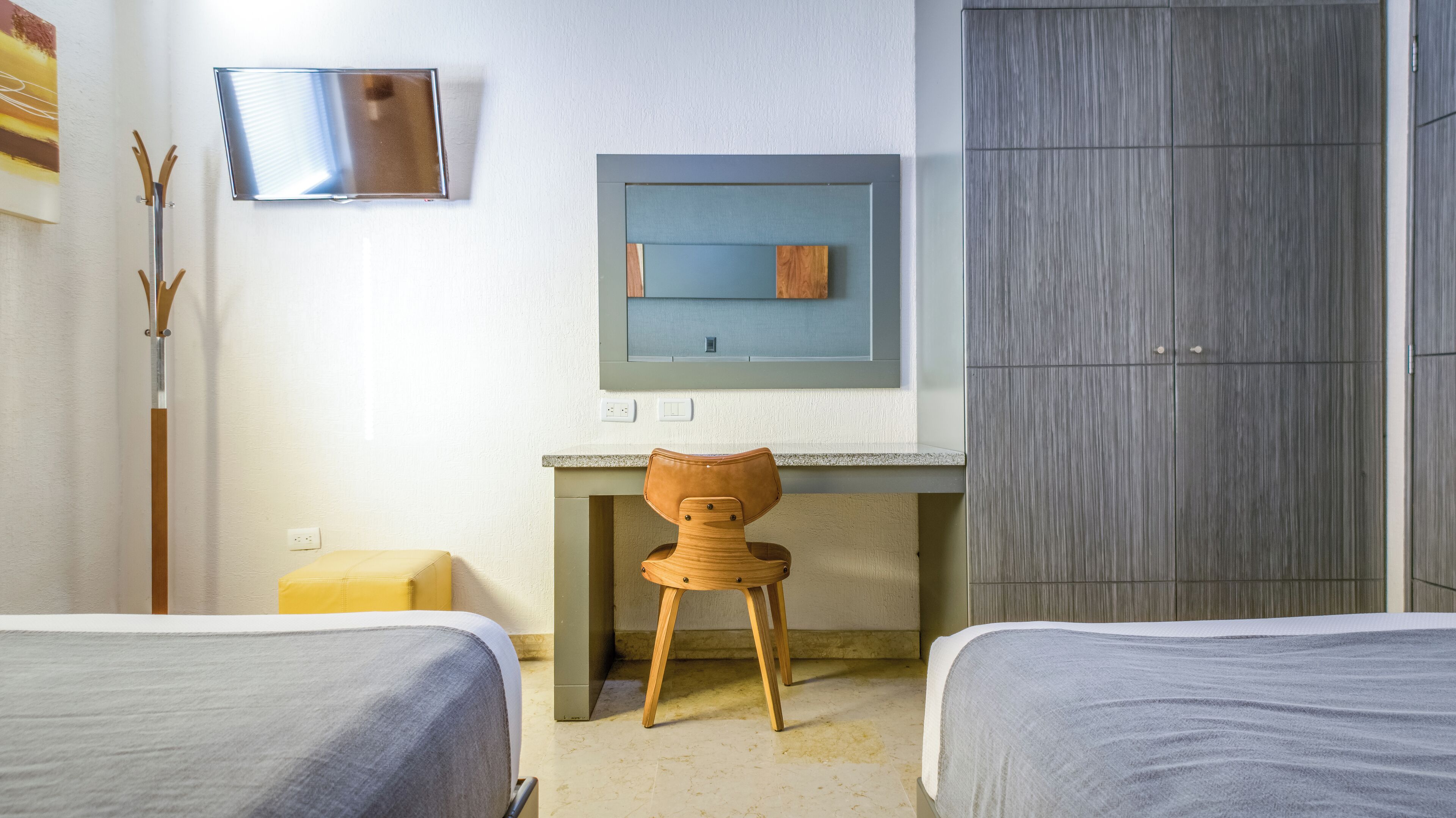 Habitación de hotel con dos camas, un escritorio con silla, un televisor montado en la pared y un armario.
