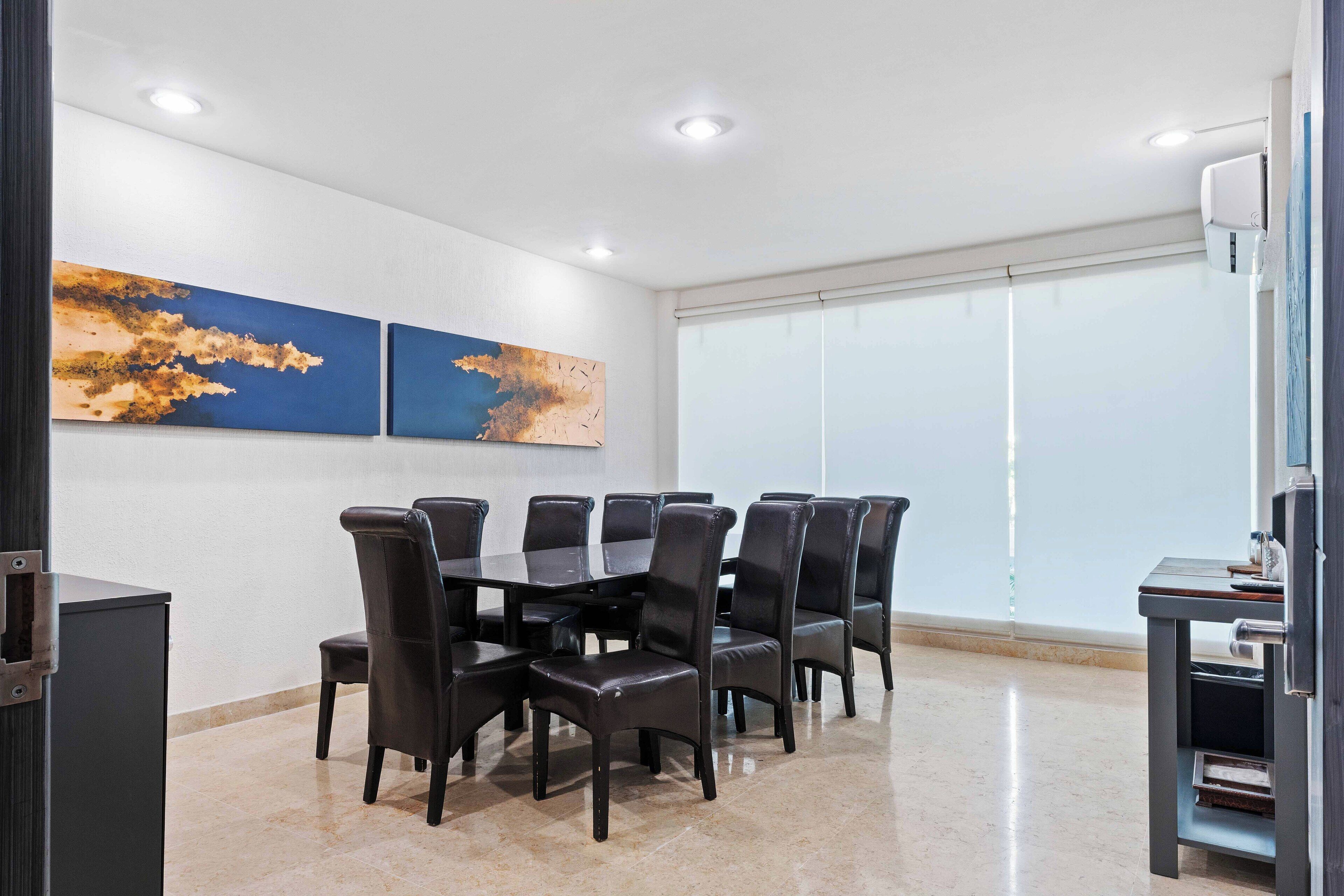 Une salle de conférence avec une grande table, des chaises noires et deux tableaux abstraits accrochés au mur.