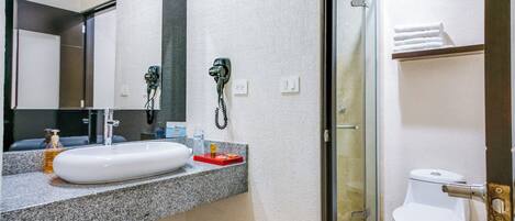 Un baño con lavamanos blanco, espejo, secador de pelo y ducha.