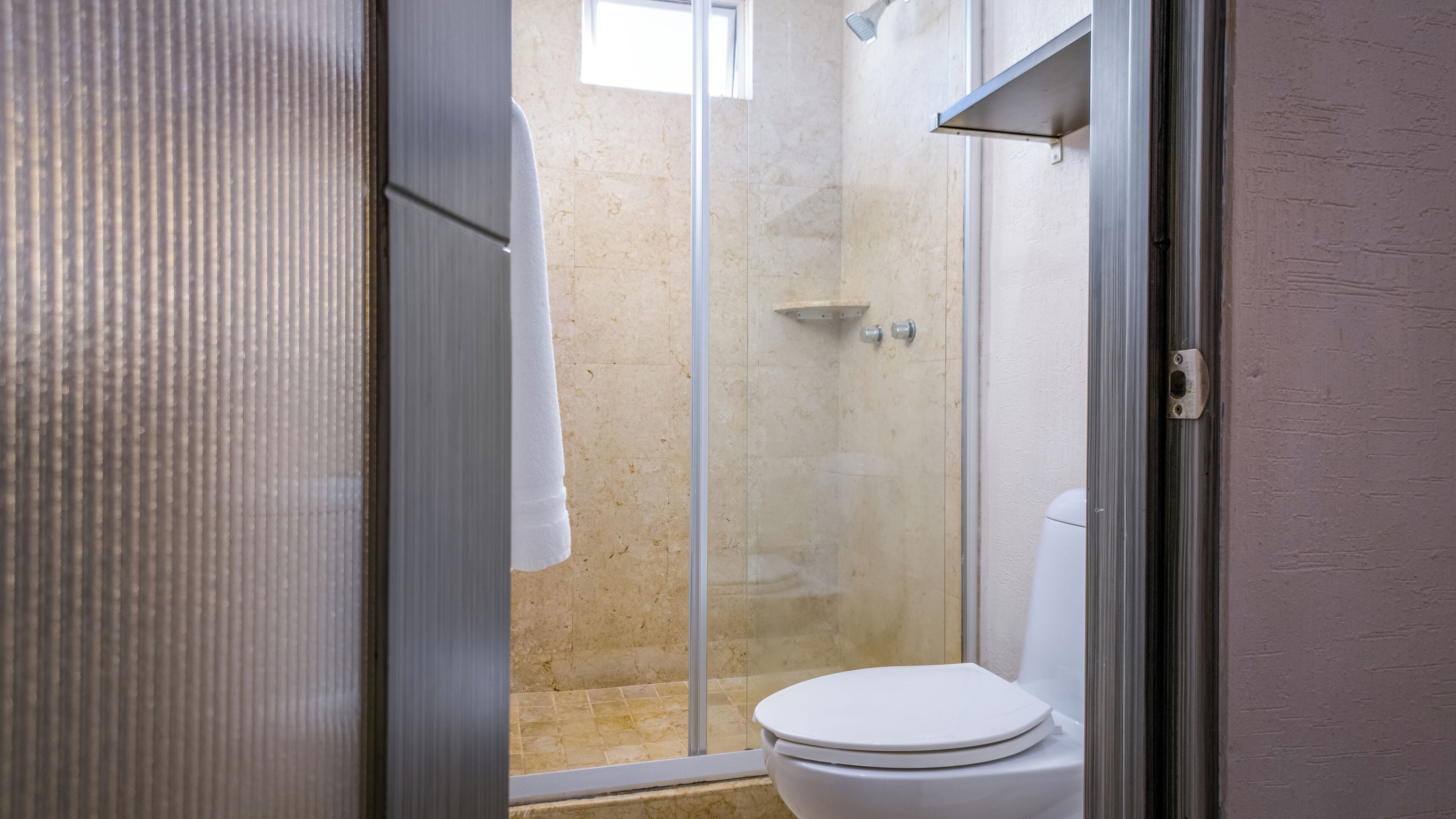 Un baño con ducha de vidrio, inodoro blanco y toalla en un perchero.