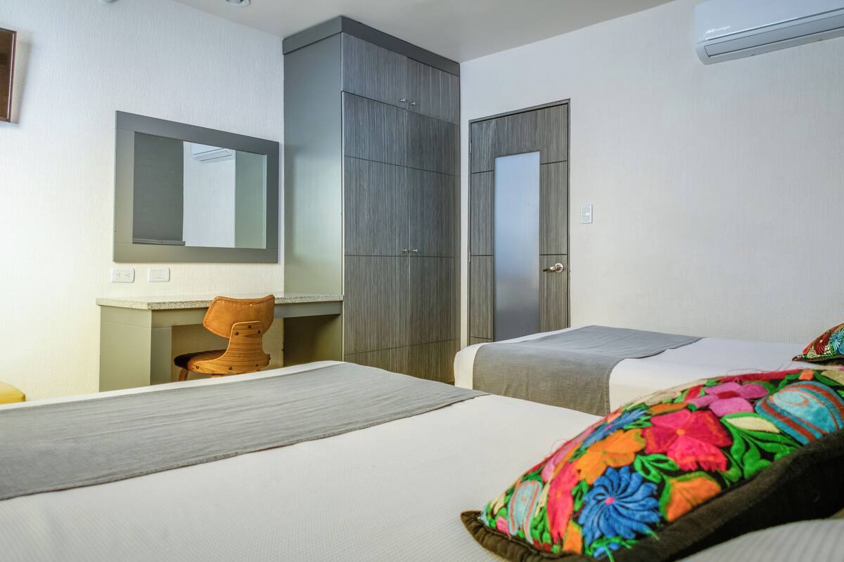 A hotel room with a bed, a desk, a chair, a wardrobe, and a mirror.