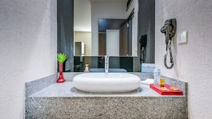 A bathroom with a granite countertop, a white sink, a red vase with green plants, a bottle of hand soap, and a red tray with a toothbrush and toothpaste. - Home Suites Rotarismo (Culiacán)