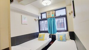 A hotel room with two single beds, a window with curtains, a wall-mounted air conditioner, and a ceiling light. - Apple Hostel (Kowloon)