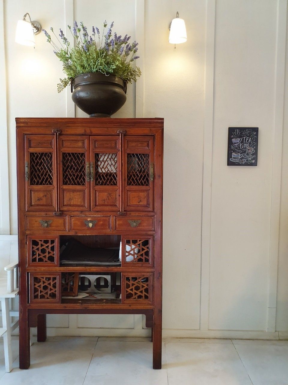 A wooden cabinet with multiple drawers and compartments, a potted plant on top, and a chalkboard with writing on the wall.