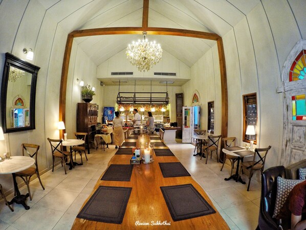 A spacious hotel lobby with a high ceiling, wooden beams, a chandelier, and a central dining area with tables and chairs. - Tharaburi Resort Sukhothai (Sukhothai)