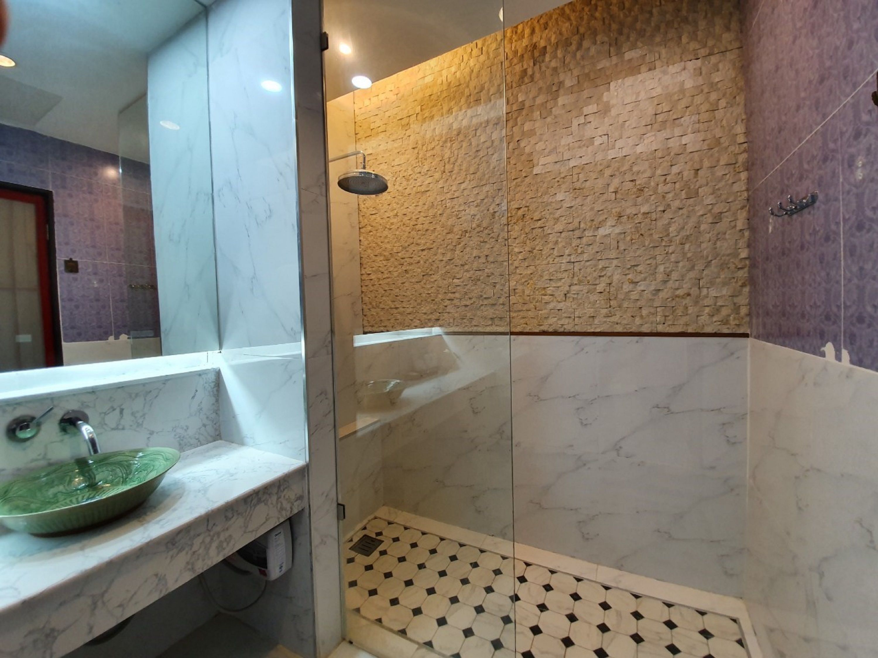 A bathroom with a marble sink, a shower with a textured wall, and a patterned floor.
