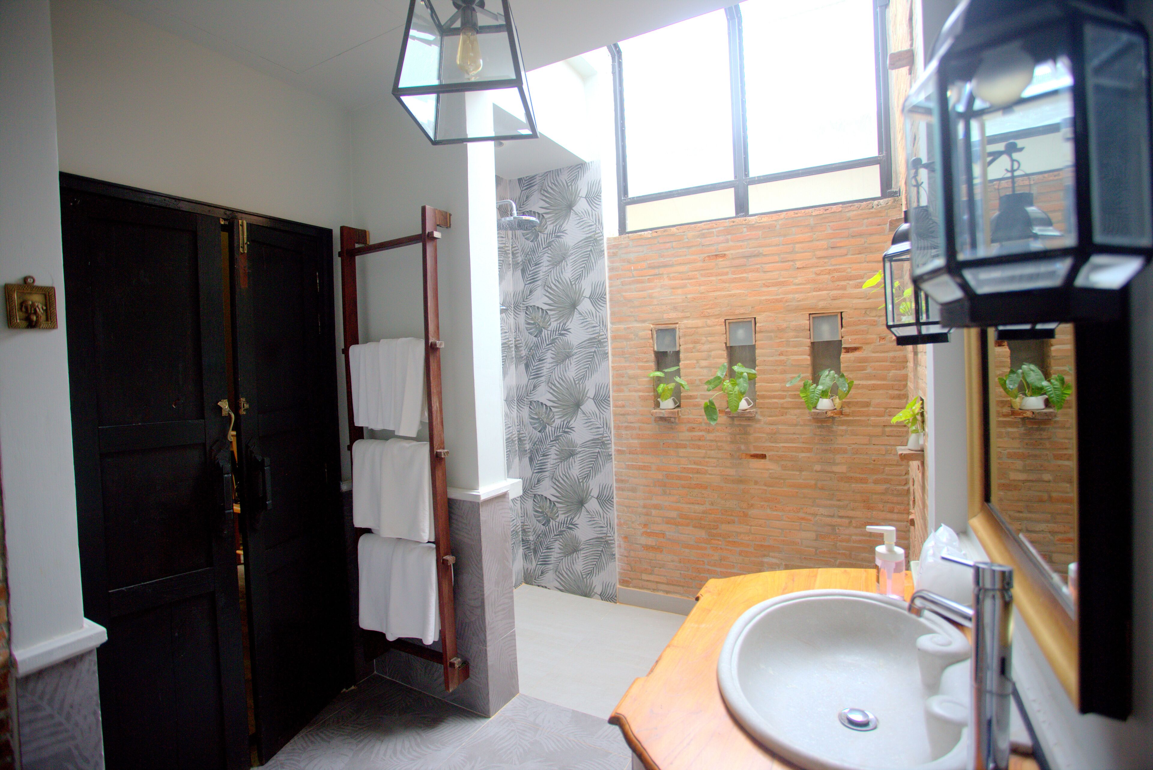 Un baño con puerta negra, toallero de madera, lavabo blanco y espejo.