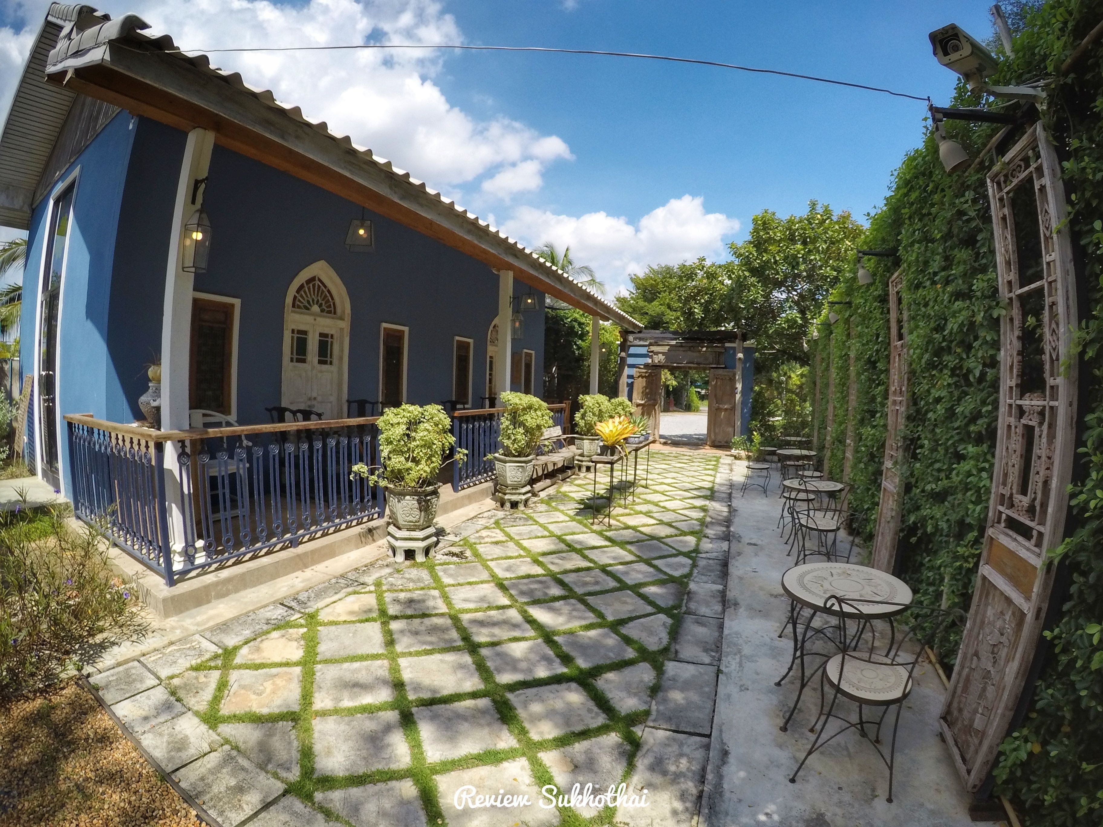 Un patio con un edificio azul, plantas en macetas y mobiliario exterior.