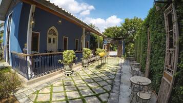 Un patio con un edificio azul, plantas en macetas y mobiliario exterior.