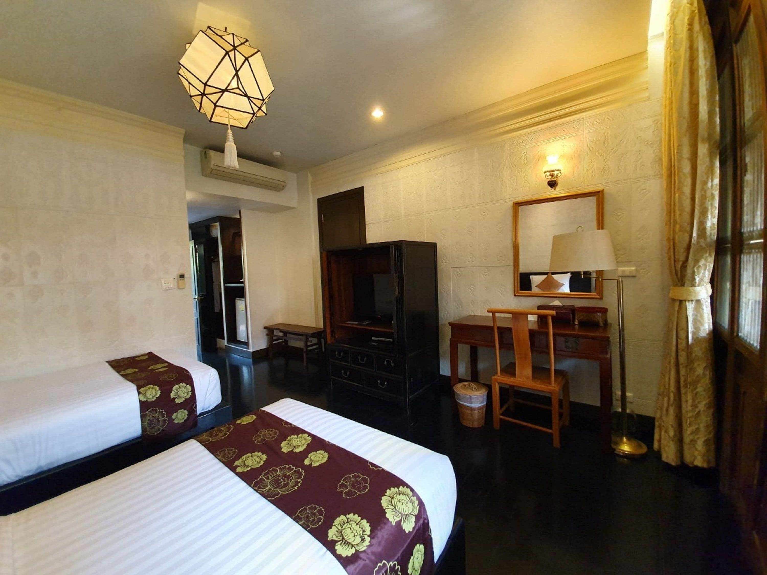 A hotel room with two beds, a desk, a television, and a mirror.