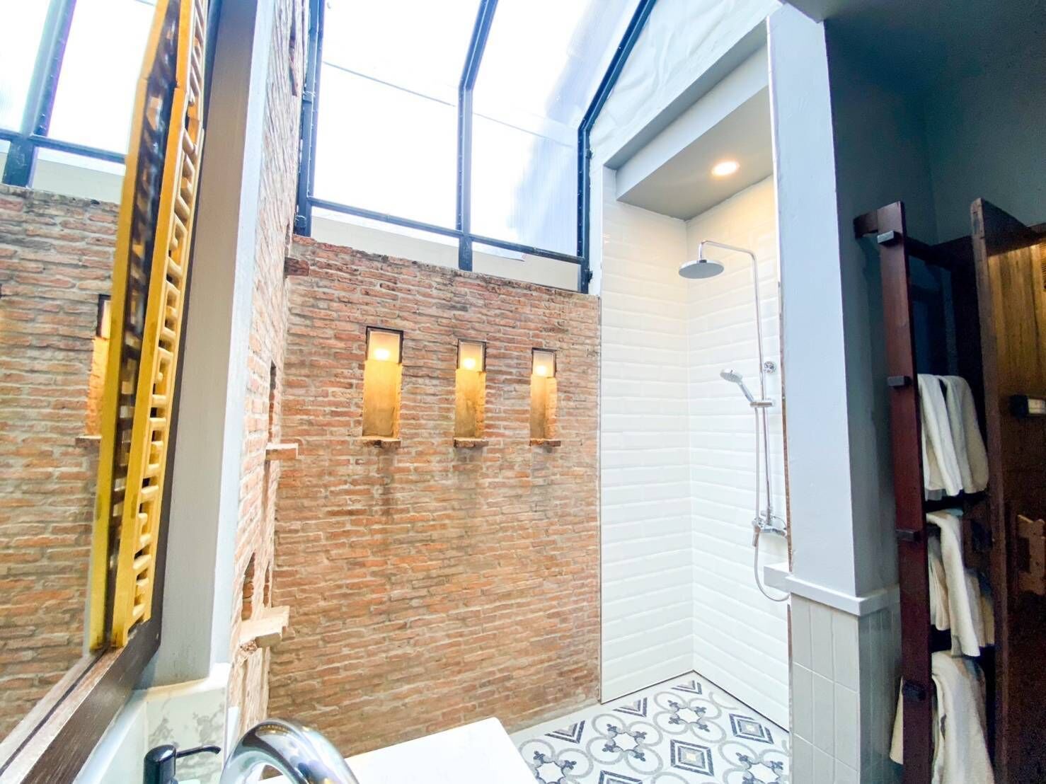 A bathroom with a brick wall, a shower, and a large skylight.