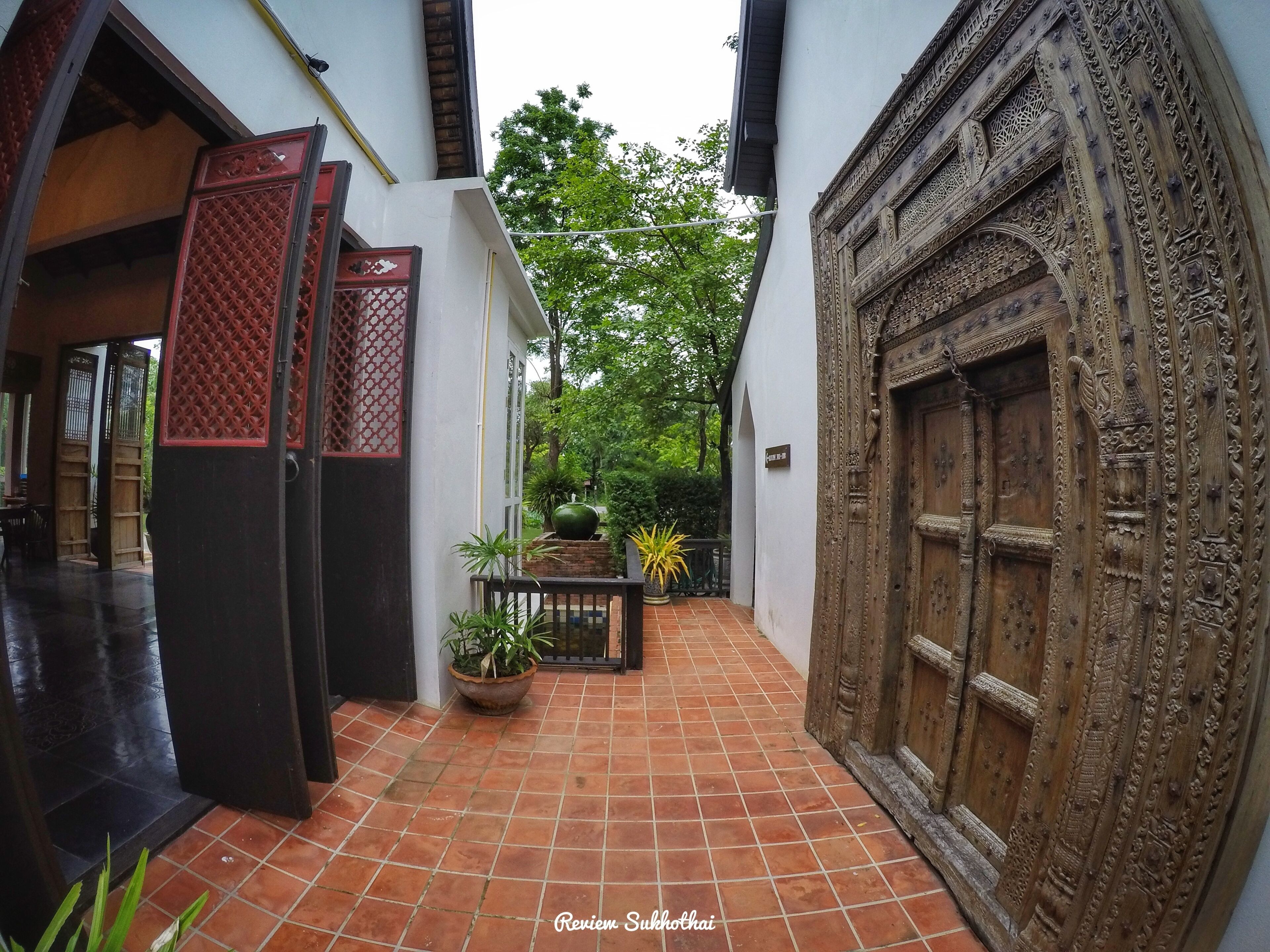 A courtyard with a tiled floor, a wooden door with intricate carvings, and a potted plant.