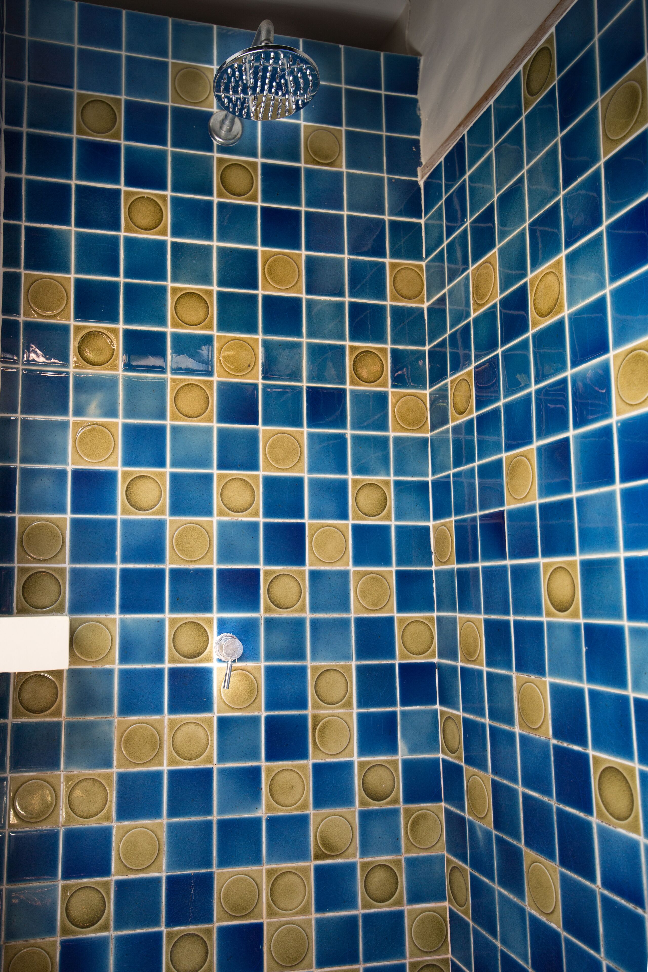 Une salle de bain avec des murs recouverts de carreaux bleus et dorés et un pommeau de douche.