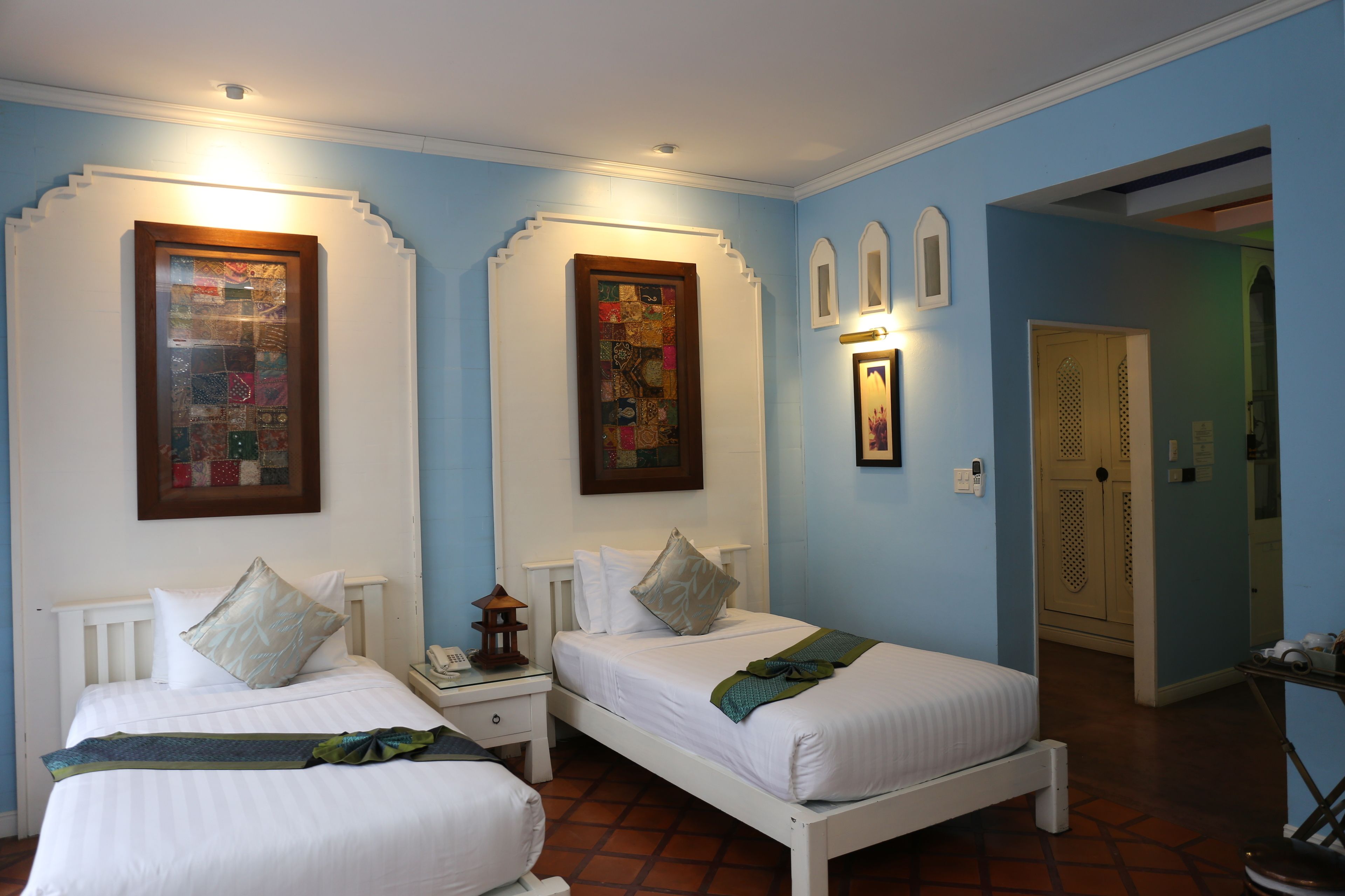 A bedroom with two beds, a nightstand, a wall-mounted phone, and a door leading to another room.