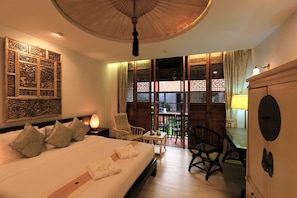 A hotel room with a large bed, a desk, and a balcony with wooden lattice. - Tharaburi Resort Sukhothai (Sukhothai)