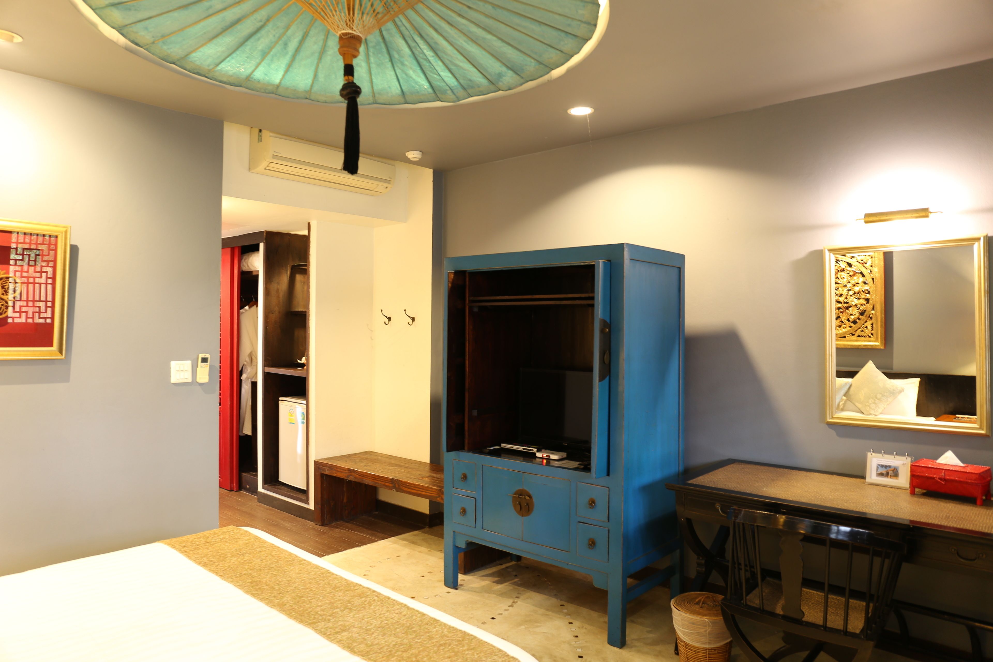 A hotel room with a bed, a desk, a wardrobe, a mirror, and a ceiling fan.
