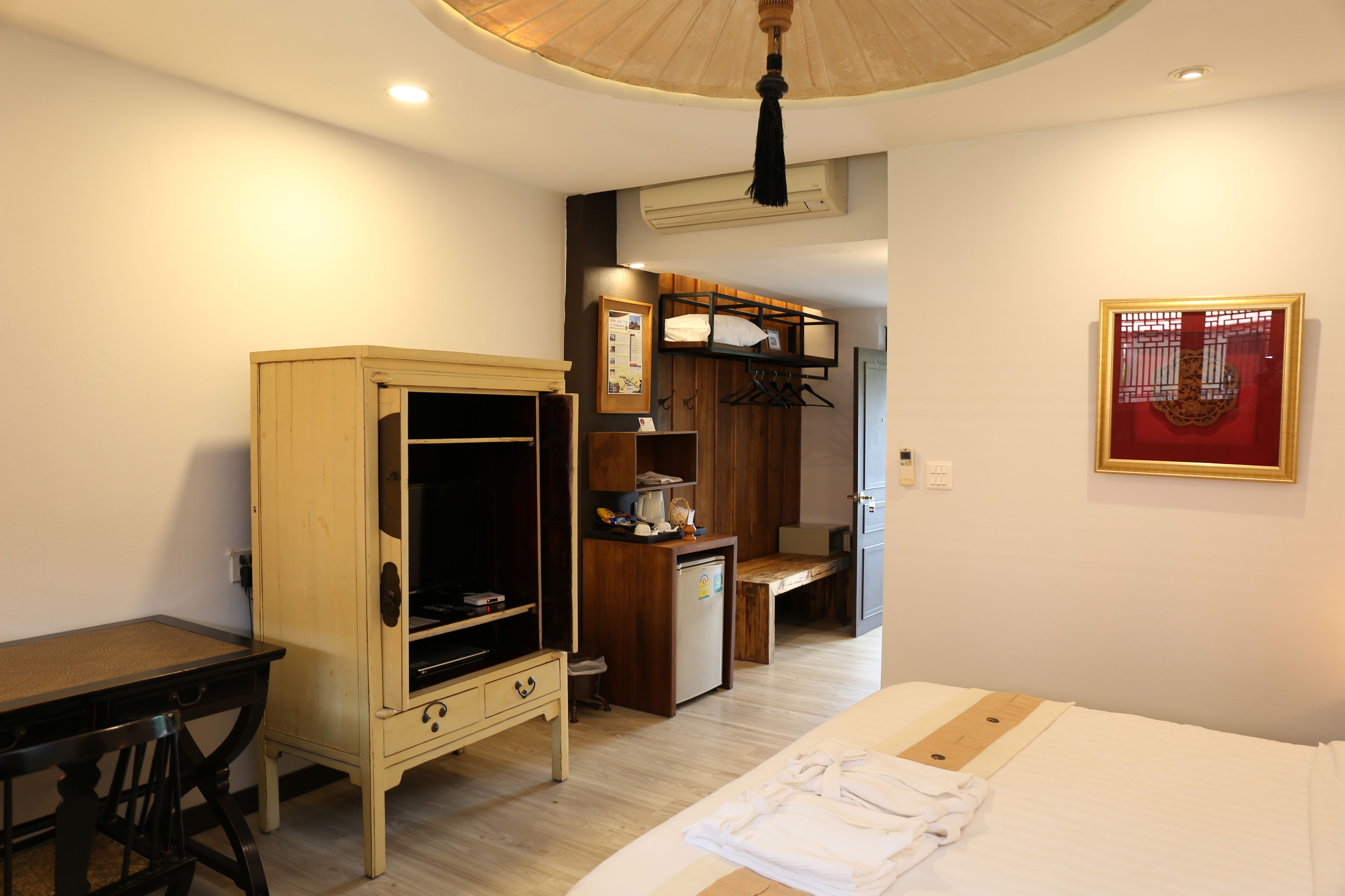 A compact hotel room with a bed, a desk, a wardrobe, and a kitchenette.