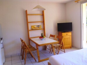 A room with a bed, a table with chairs, a television on a wooden cabinet, and a shelf with a painting. - Hotel Résidence BEAR (Port-Vendres)