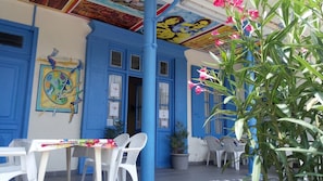 A blue building with a colorful mural, white plastic chairs, and a table with a colorful tablecloth. - Hotel Résidence BEAR (Port-Vendres)