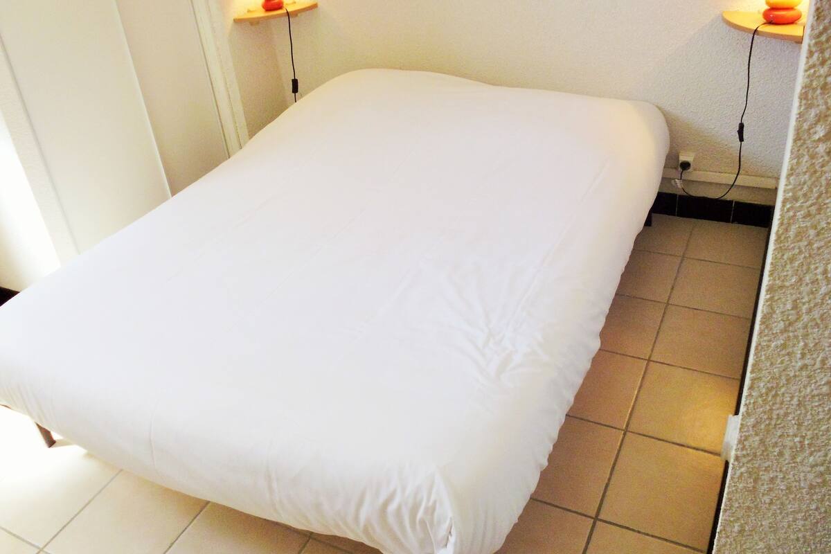 A single bed with a white mattress in a room with tiled flooring.