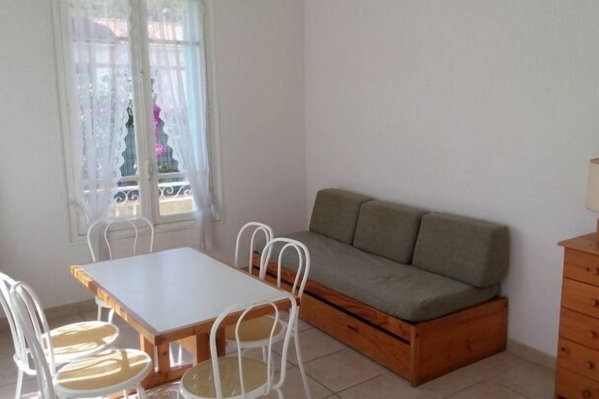 A room with a wooden sofa, a dining table with chairs, a wooden dresser, and a window with curtains.