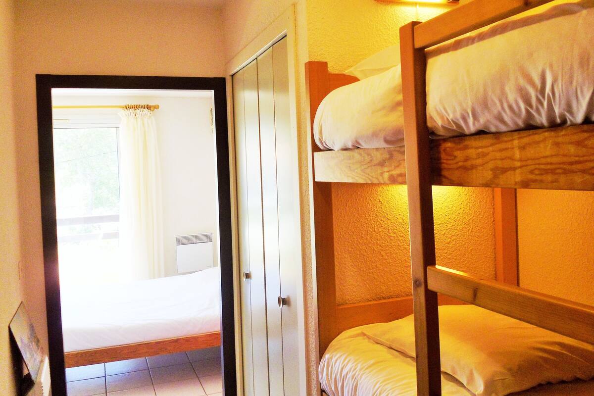 A room with a bunk bed, a door leading to another room, and a window with curtains.