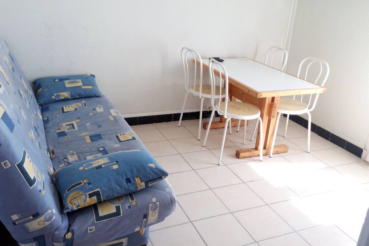 A small room with a blue patterned sofa, a wooden table with white chairs, and white tiled flooring.