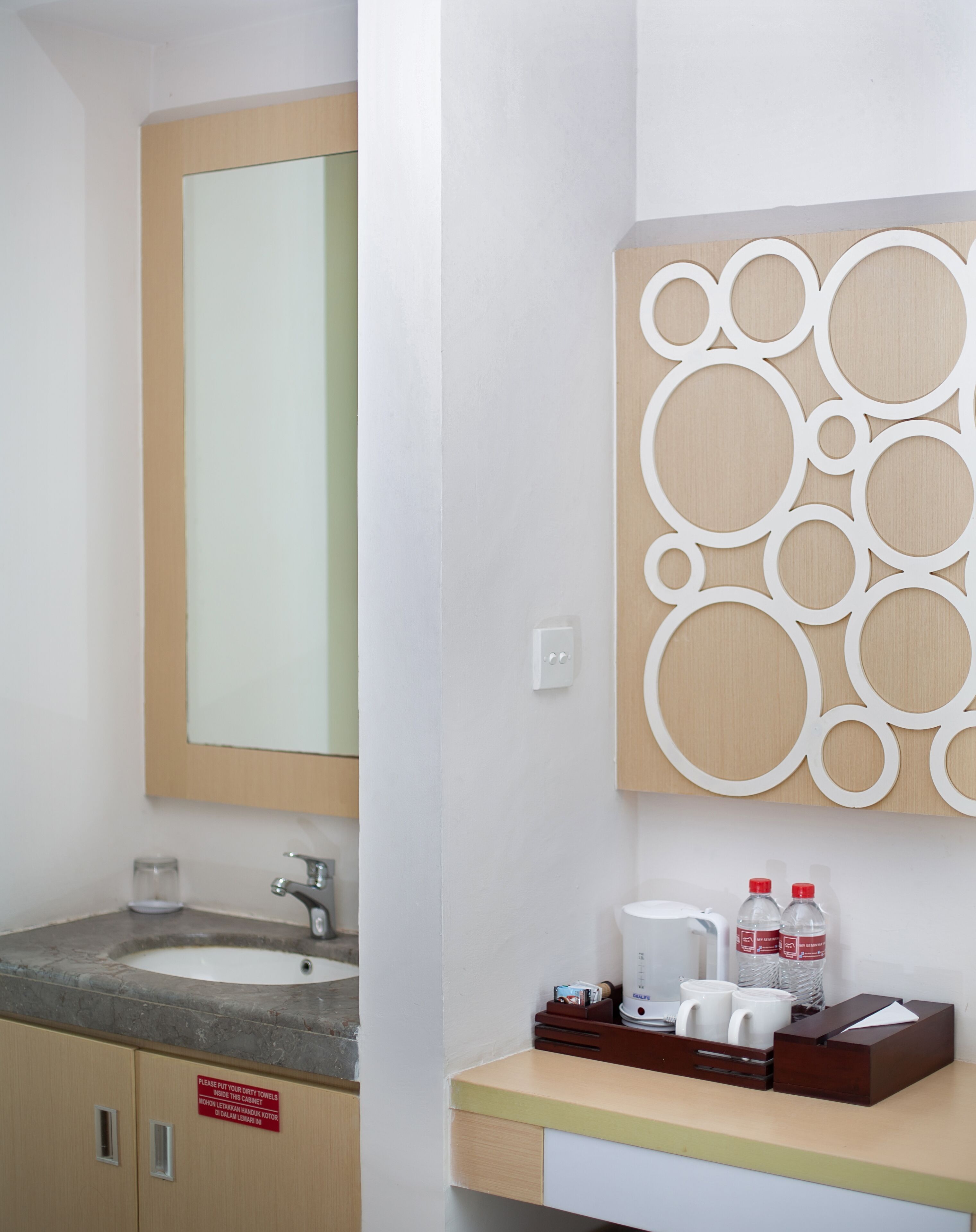A bathroom with a sink, mirror, and decorative wall panel. There are toiletries on the counter.
