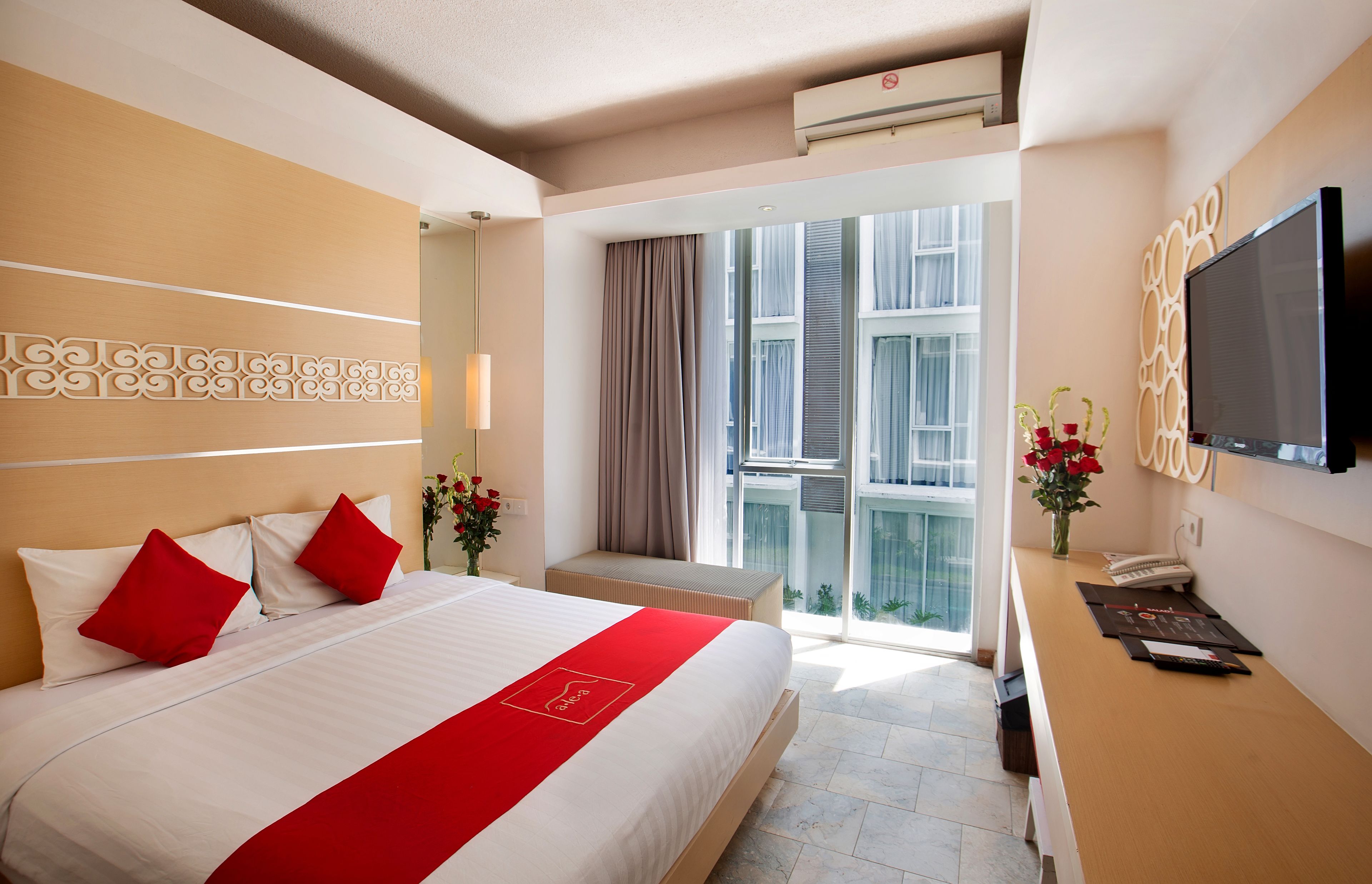 A hotel room with a large bed, a desk with a flat-screen TV, and a balcony with a view of the city.