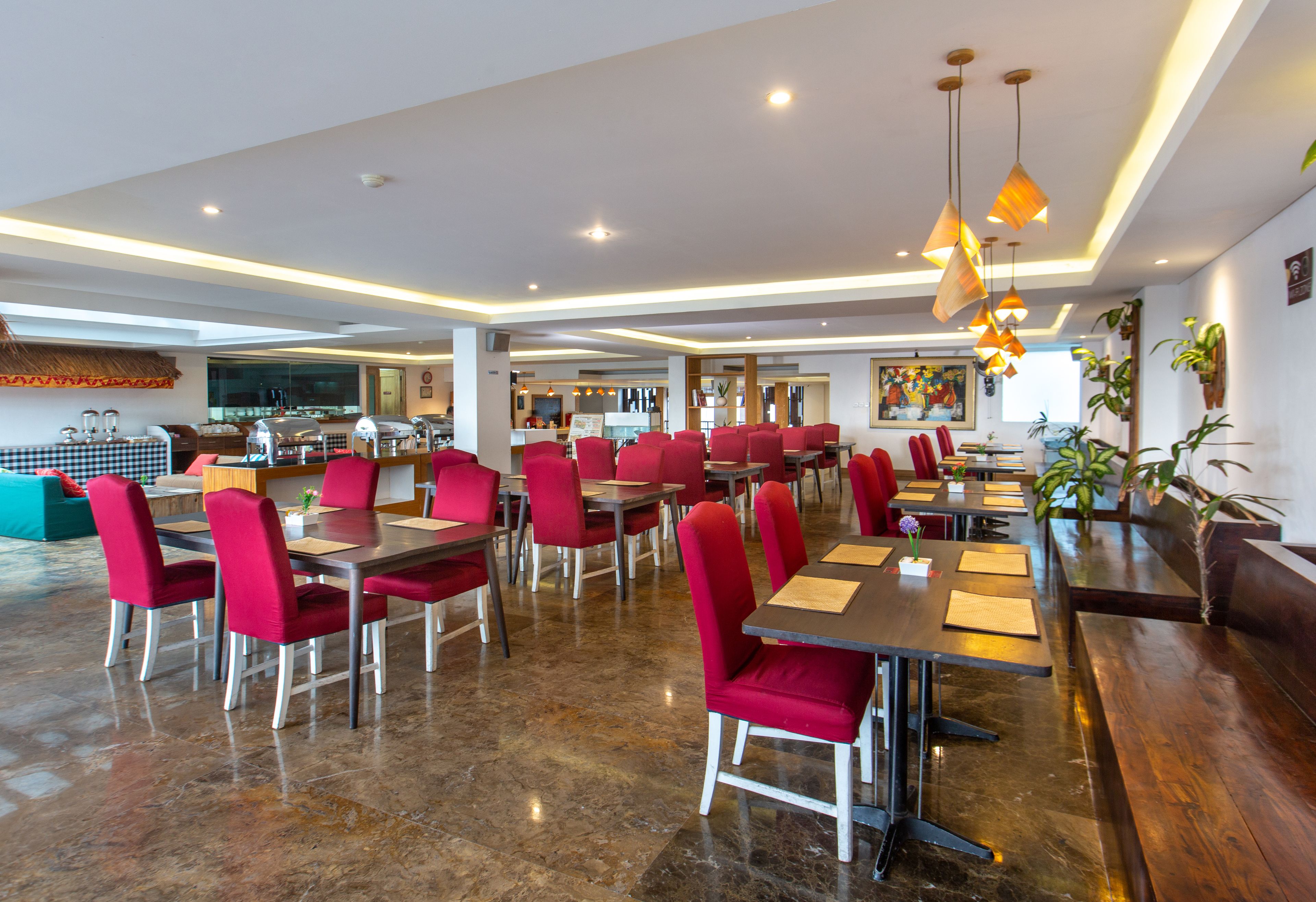 Un restaurante espacioso con sillas rojas y mesas de madera, una zona de bar y una cocina al fondo.