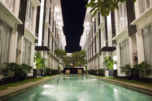 A pool area with a central water feature, flanked by symmetrical buildings with large windows and potted plants.