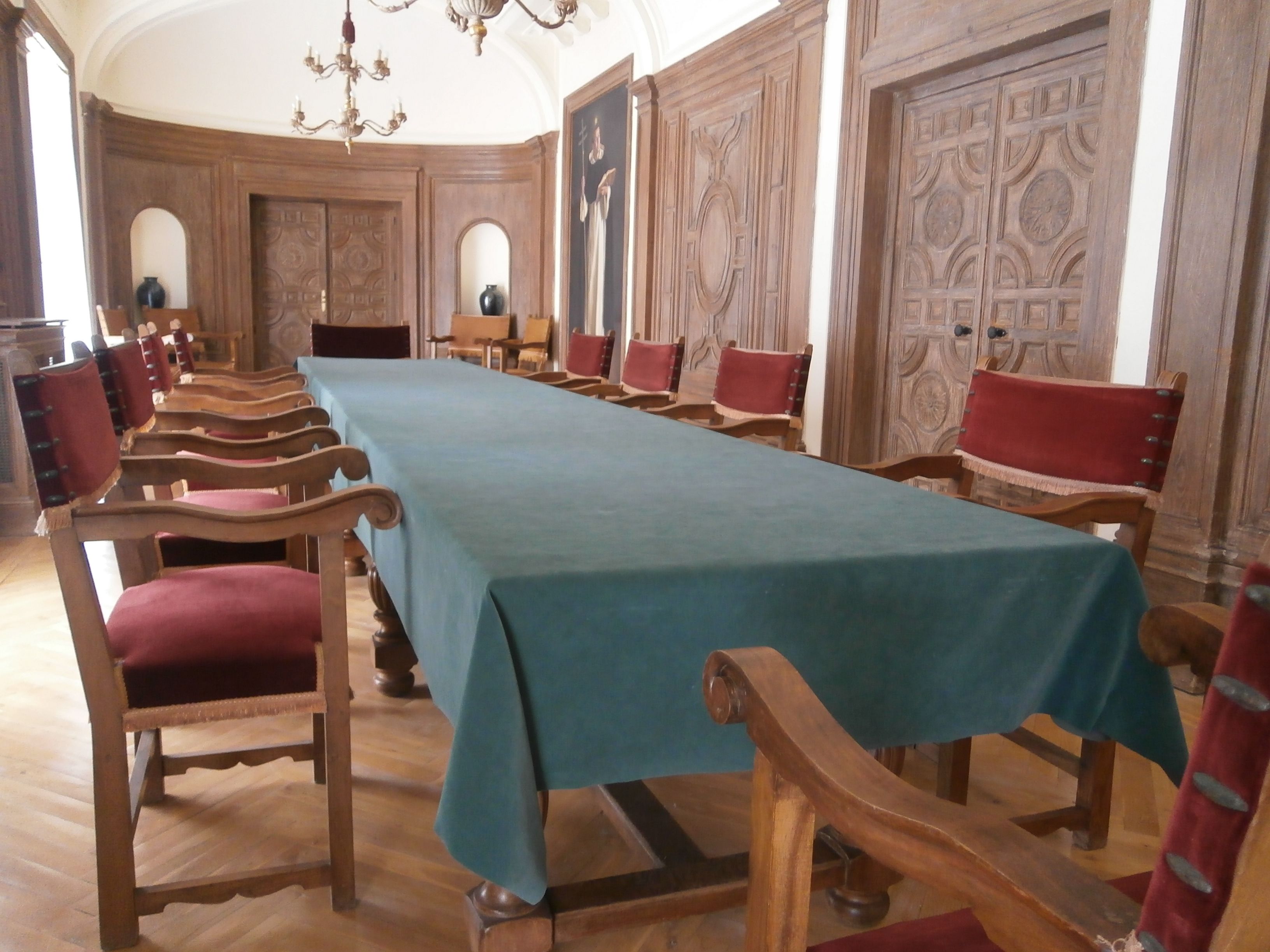 Un salón de conferencias con una larga mesa, sillas de madera y puertas de madera decoradas.