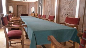 Un salón de conferencias con una larga mesa, sillas de madera y puertas de madera decoradas.