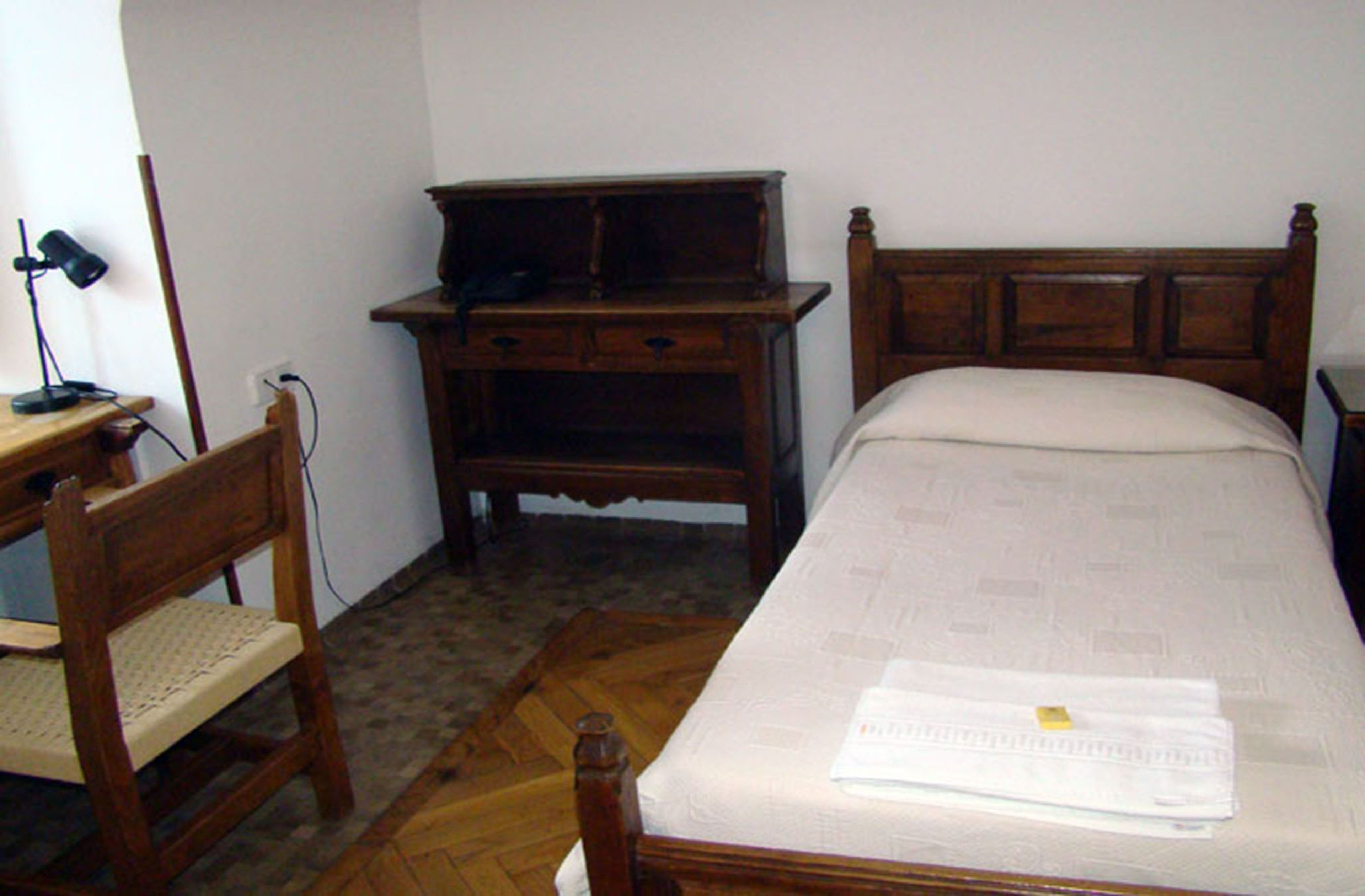 A bedroom with a wooden bed, a nightstand, a desk with a chair, and a lamp.