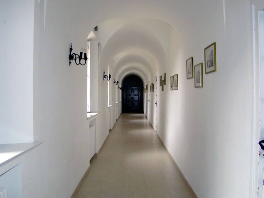 A long, narrow hallway with white walls and a tiled floor, leading to a dark doorway at the end.
