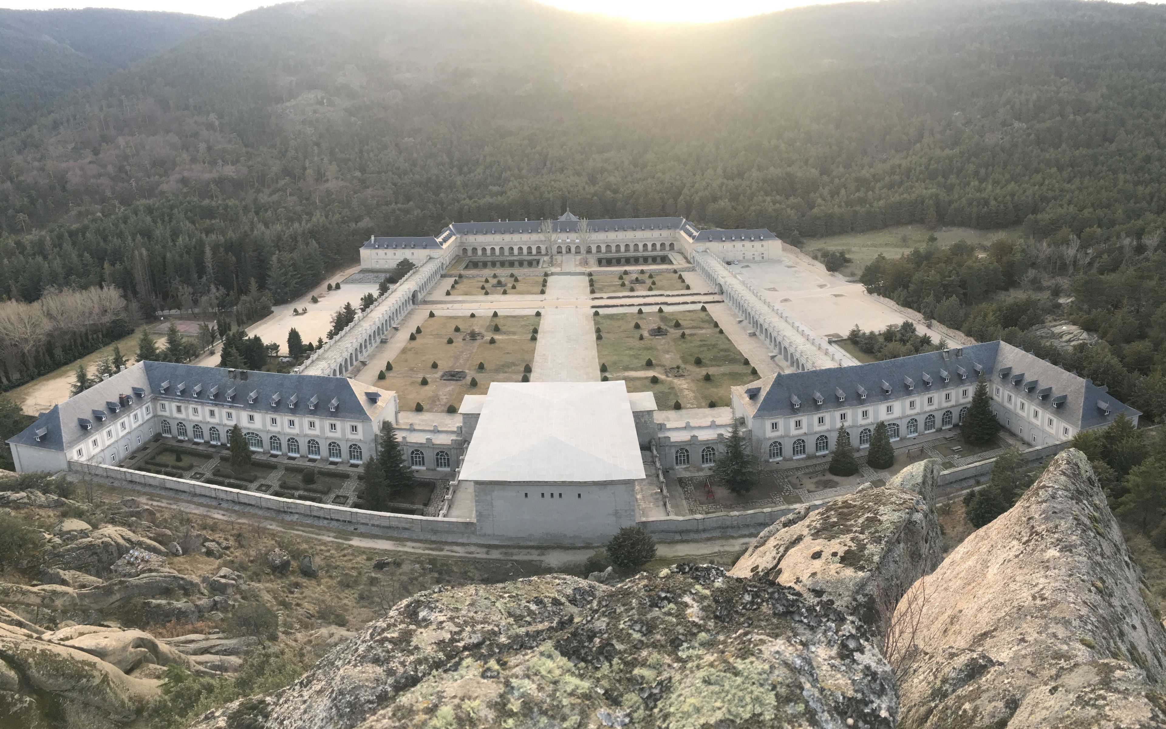 A large, symmetrical building with a central courtyard, surrounded by a high wall and set in a mountainous area.