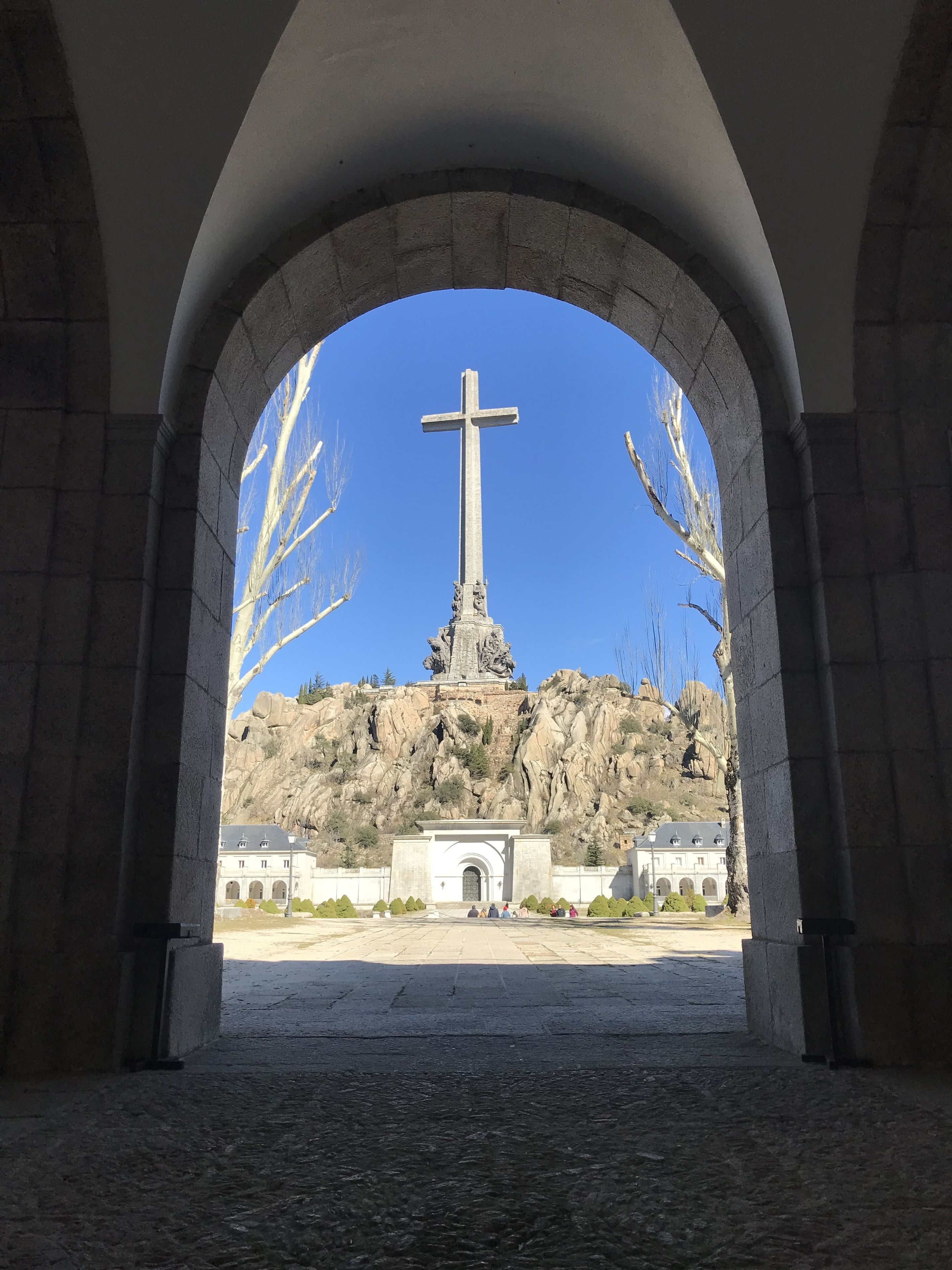An archway framing a cross monument with a building in the background.