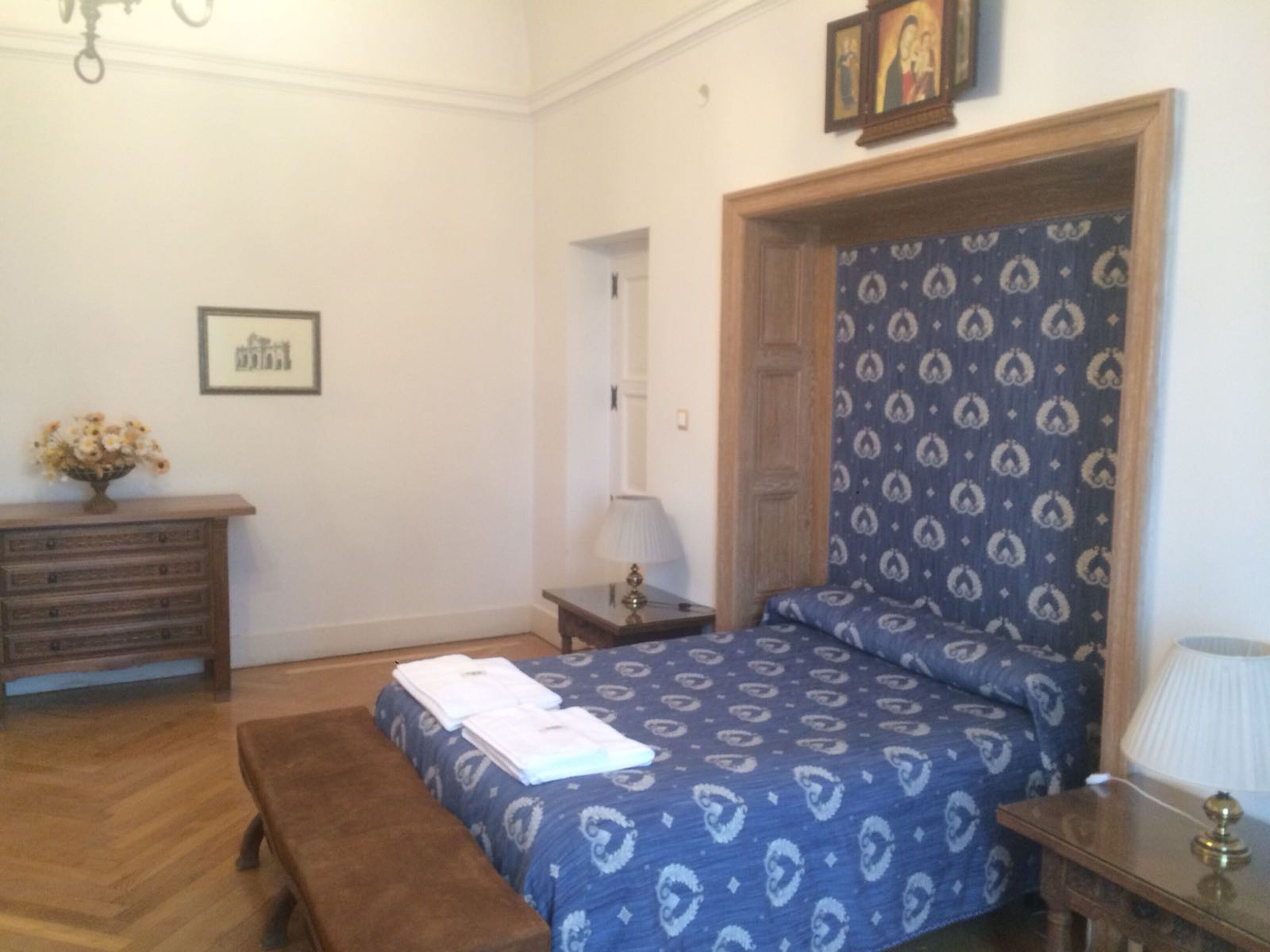 Ein Schlafzimmer mit einem hölzernen Bett, einer Holzbank, einem Schminktisch, einer Lampe und einem gerahmten Bild an der Wand.